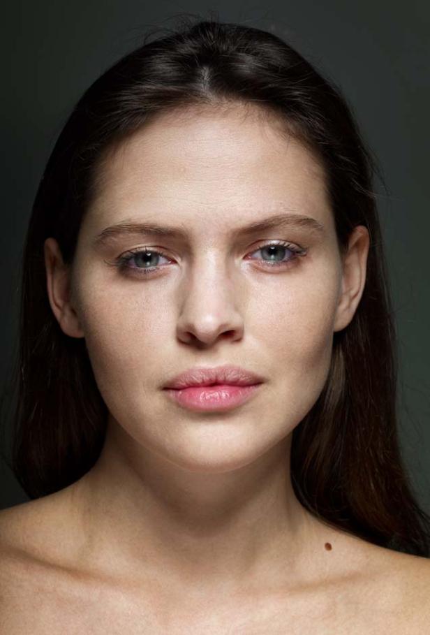 Porträt einer jungen Frau mit braunen Haaren und hellen Augen vor dunklem Hintergrund.