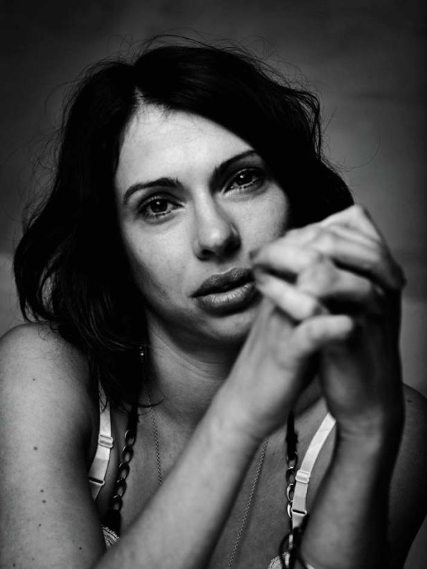 Schwarzweißporträt einer Frau mit dunklen Haaren, die ihre Hände vor dem Gesicht verschränkt.