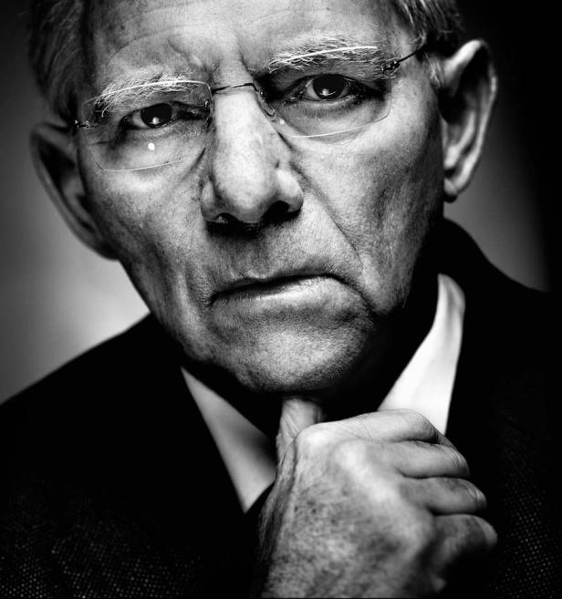 Ein Schwarzweißporträt eines älteren Mannes mit Brille, der nachdenklich sein Kinn berührt.