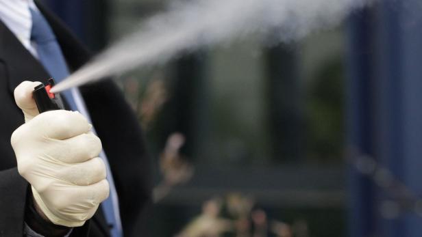 Eine Person in Anzug und Handschuhen sprüht Pfefferspray.