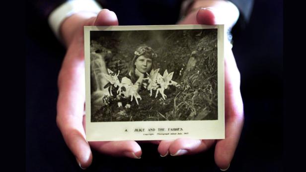 Eine Person hält ein historisches Foto mit einem Mädchen und Feen in den Händen.