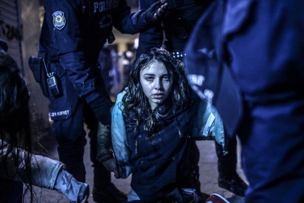 Eine junge Frau mit Tränen in den Augen wird von Polizisten abgeführt.