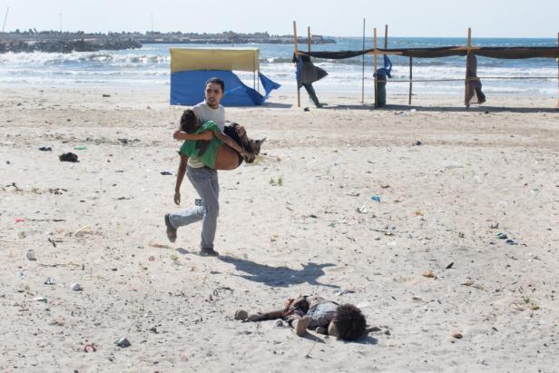 Ein Mann trägt ein Kind am Strand weg, während ein anderes Kind am Boden liegt.