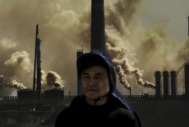 Ein Mann steht vor einer Fabrik, aus der Rauch aufsteigt.