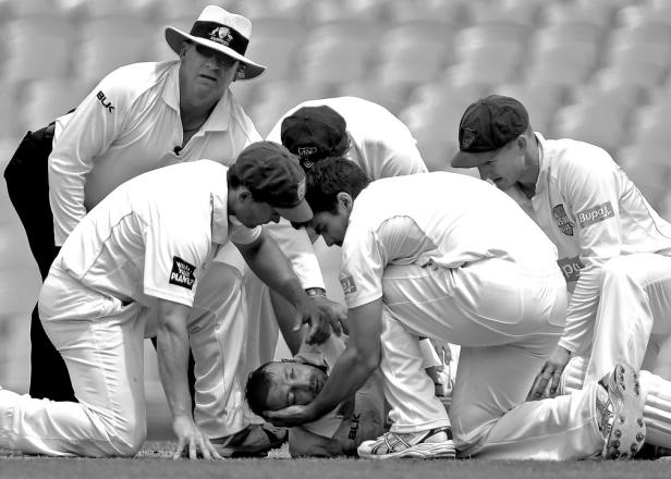 Cricket-Spieler kümmern sich um einen verletzten Spieler auf dem Feld.