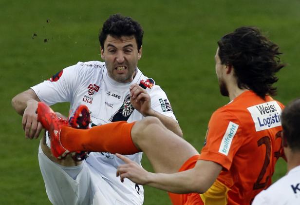 Ein Fußballspieler wird von einem anderen gefoult, wobei Dreck aufwirbelt.