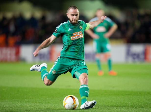 Ein Fußballspieler in grüner Uniform schießt einen Ball.