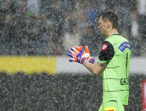 Ein Torwart steht im Regen mit Handschuhen auf dem Fußballfeld.