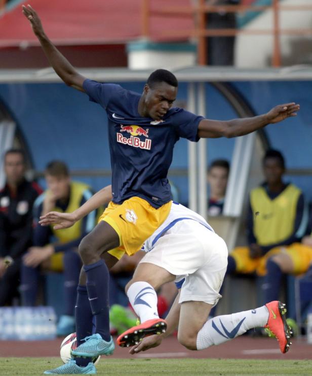 Ein Fußballspieler im dunkelblauen Trikot von Red Bull dribbelt den Ball, während ein Gegenspieler zu Fall kommt.