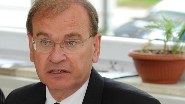 Ein Mann mit Brille und dunklem Anzug sitzt an einem Tisch.