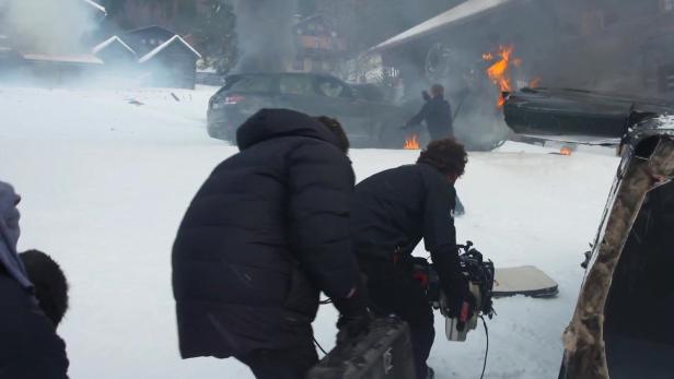Ein Filmteam dreht eine Szene mit brennenden Autos in einer verschneiten Landschaft.