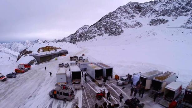 Ein Filmset mit LKWs und Ausrüstung in einer verschneiten Berglandschaft.