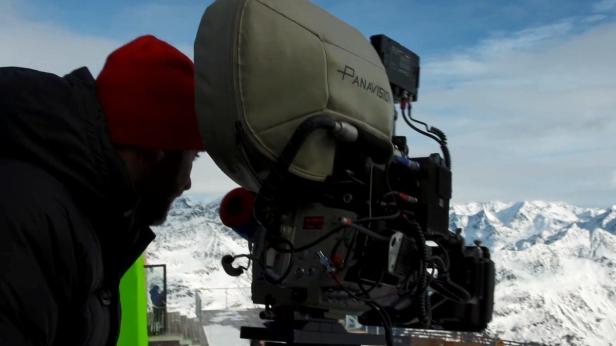 Ein Kameramann filmt mit einer Panavision-Kamera vor einer verschneiten Bergkulisse.