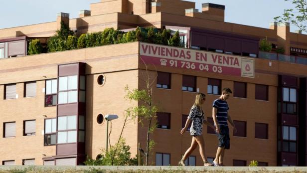 Ein Paar geht an einem Wohnhaus mit dem Schild „Viviendas en Venta“ vorbei.