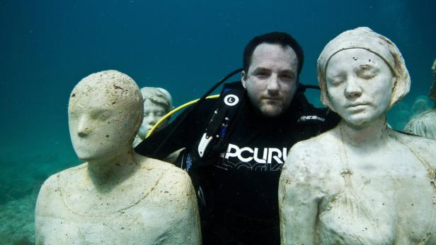 Ein Taucher inmitten von Skulpturen unter Wasser.