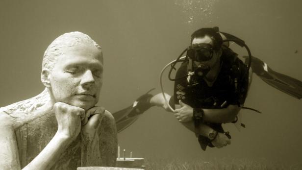 Ein Taucher schwimmt neben einer Skulptur unter Wasser.