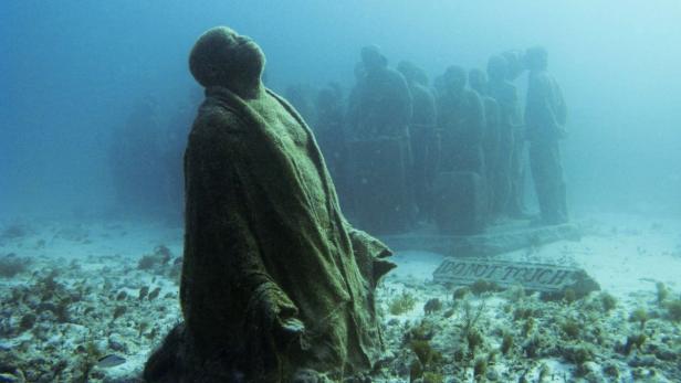 Unterwasser-Statuen stehen auf dem Meeresgrund, bewachsen mit Algen.