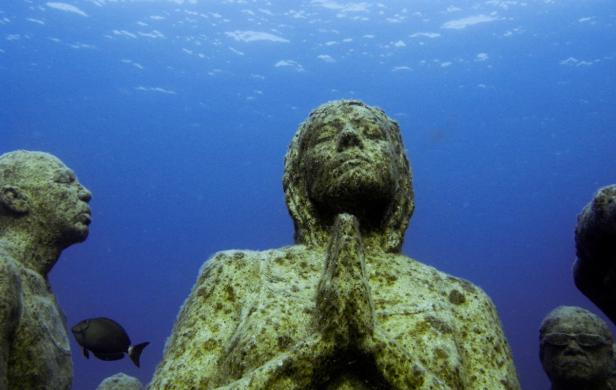 Unterwasser-Skulpturen, die von Algen und Korallen bewachsen sind.