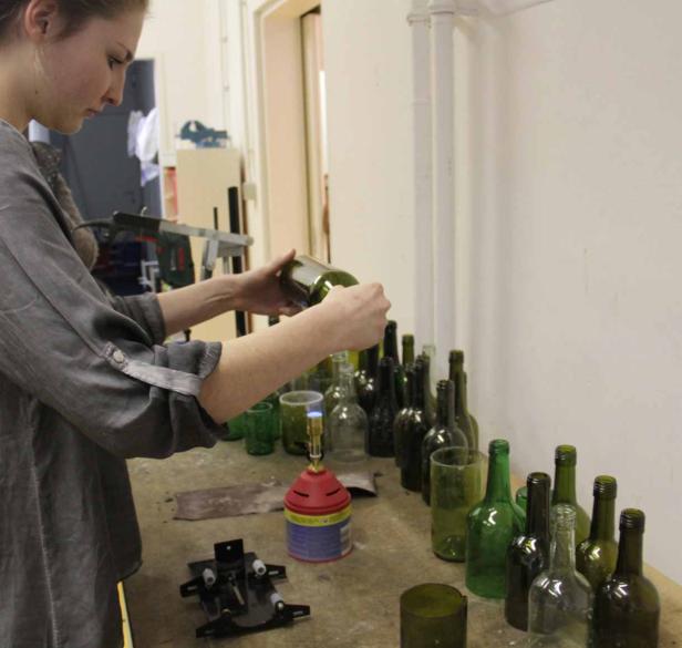 Eine Frau bearbeitet eine grüne Glasflasche mit einem Brenner.