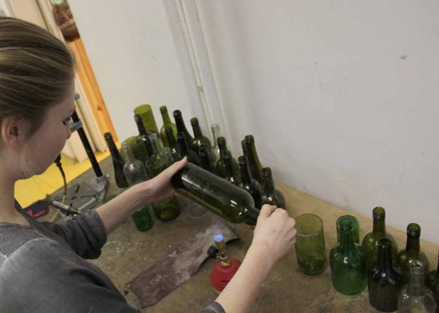 Eine Frau bearbeitet eine grüne Glasflasche mit einem Brenner.