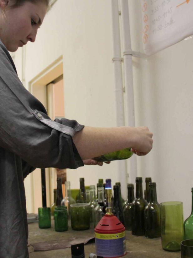Eine Person bearbeitet eine grüne Glasflasche mit einem Brenner.