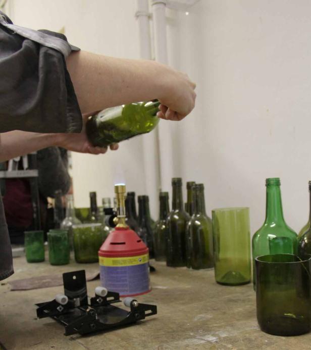 Eine Person erhitzt eine grüne Glasflasche mit einem Brenner, um sie zu bearbeiten.