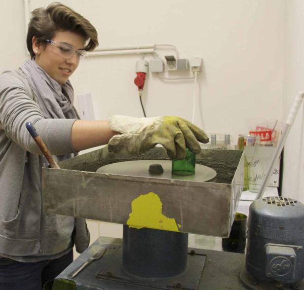Eine Frau schleift ein grünes Glasgefäß mit einer Poliermaschine.