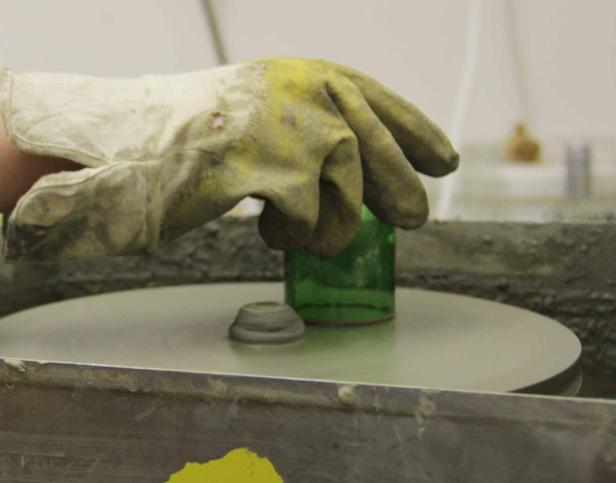 Eine Hand mit Handschuh poliert eine grüne Glasflasche auf einer Schleifscheibe.