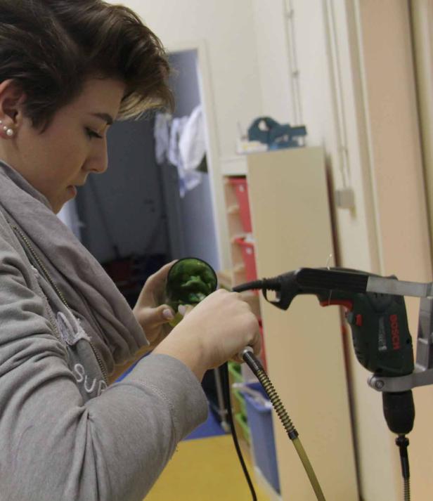 Eine Frau bearbeitet ein grünes Glasobjekt mit einem Werkzeug.