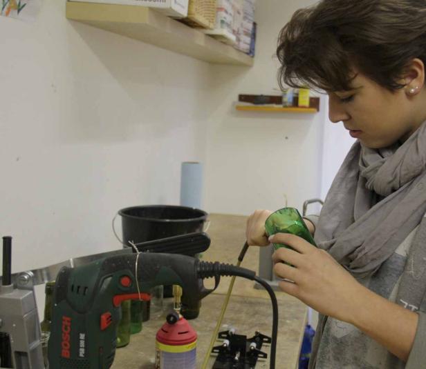 Eine Frau bearbeitet eine grüne Glasflasche mit Werkzeugen.