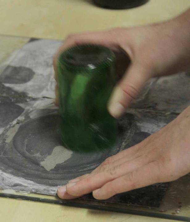 Eine Person verwendet eine grüne Glasflasche, um Farbe auf einer Oberfläche zu verteilen.