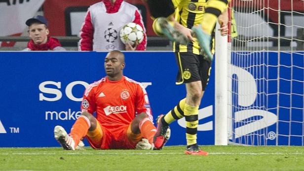 Ein Fußballtorwart sitzt auf dem Rasen, während ein Spieler des BVB vorbeiläuft.