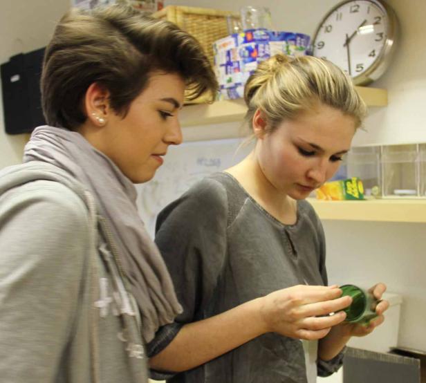 Zwei junge Frauen betrachten gemeinsam einen grünen Behälter.
