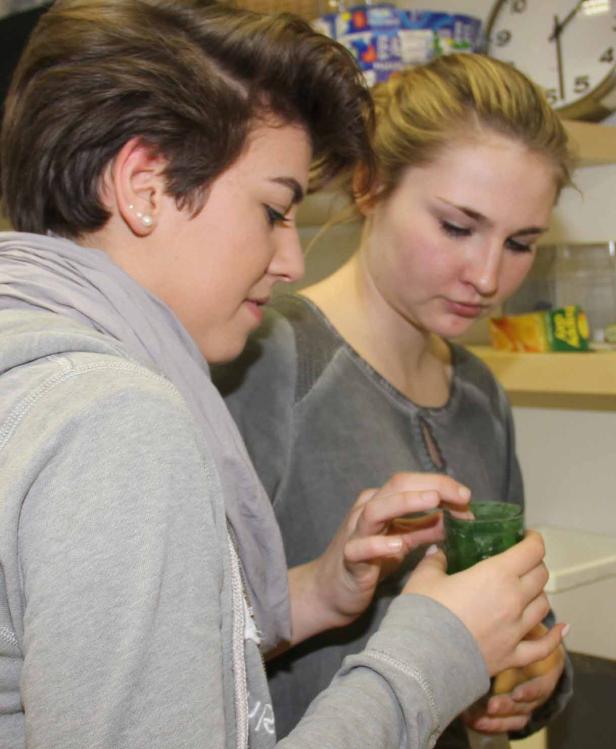 Zwei junge Frauen betrachten ein grünes Glasgefäß.