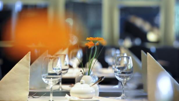 Ein gedeckter Tisch mit Weingläsern, Servietten und einer orangefarbenen Gerbera in einer Vase.