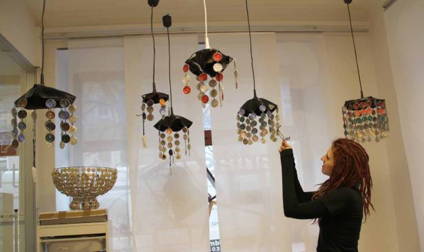 Eine Frau betrachtet Lampen und eine Schale, die mit Kaffeekapseln verziert sind.