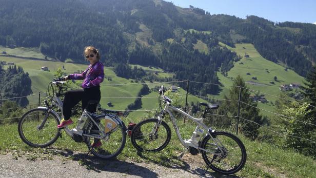 Eine Frau sitzt auf einem E-Bike vor einer grünen Hügellandschaft.