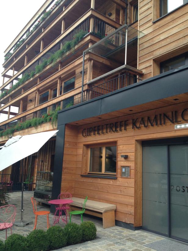 Das Holzgebäude „Gipfeltreff Kaminlo“ mit bunten Gartenmöbeln davor.