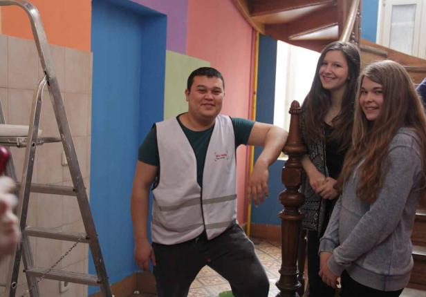 Ein Mann in Arbeitskleidung steht mit zwei jungen Frauen in einem Treppenhaus.