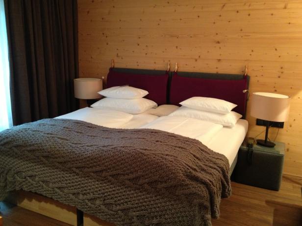 Ein Doppelbett mit einer grauen Strickdecke in einem Zimmer mit Holzvertäfelung.