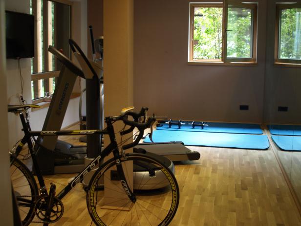 Ein Fitnessraum mit einem Fahrrad, einem Laufband und Hanteln auf blauen Matten.