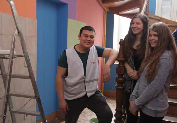 Ein Mann in Arbeitskleidung posiert mit zwei jungen Frauen in einem Treppenhaus.