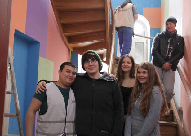 Eine Gruppe junger Leute steht in einem farbenfrohen Treppenhaus.