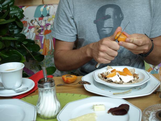 Ein Mann schneidet eine Aprikose für sein Müsli mit Joghurt.