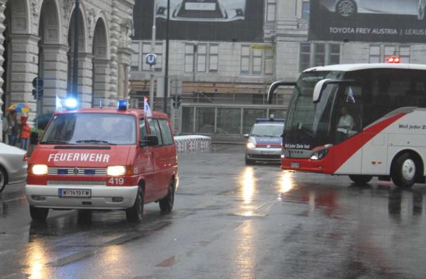 Ein roter Feuerwehrwagen und ein Bus fahren auf einer nassen Straße in Wien.
