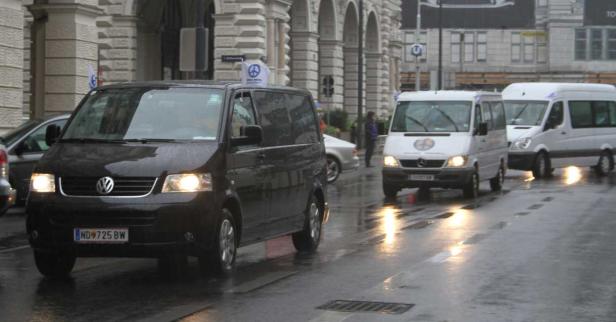 Auf einer regnerischen Straße fahren mehrere Lieferwagen.