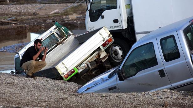 Ein Mann fotografiert die durch eine Überschwemmung beschädigten Fahrzeuge.