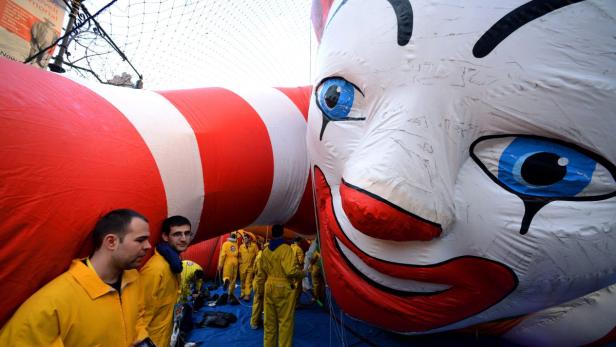 Eine riesige, aufblasbare Clownsfigur mit rot-weißen Streifen und Mitarbeitern in gelben Overalls.