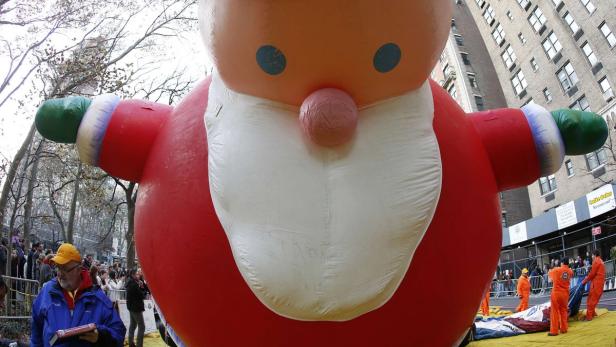 Ein riesiger, aufgeblasener Weihnachtsmann schwebt über einer Menschenmenge in einer Stadt.