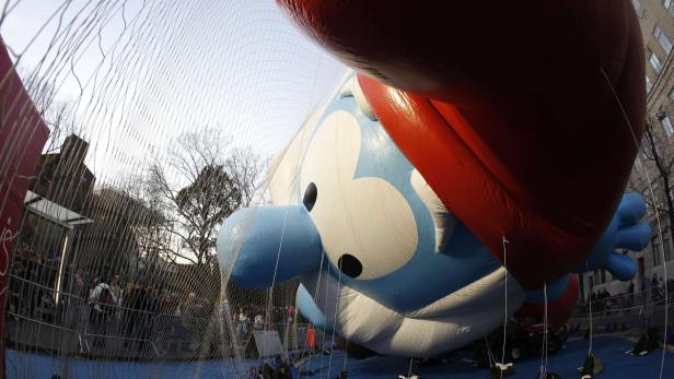 Ein riesiger Schlumpf-Ballon wird bei einer Parade von Sicherheitsleuten gehalten.